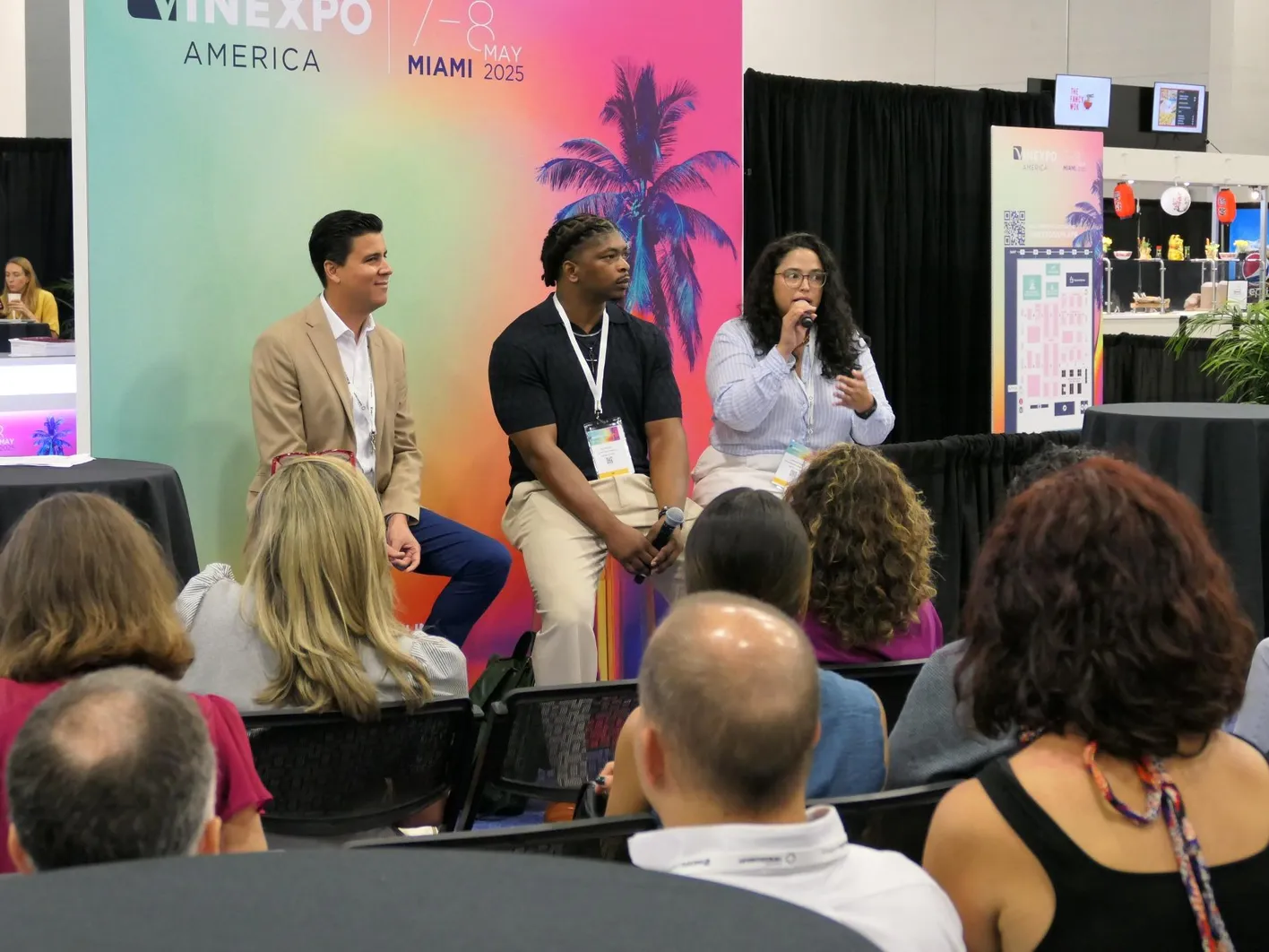 Three person as speakers during a Vinexpo Americas conference in front of a crowd of visitors.
