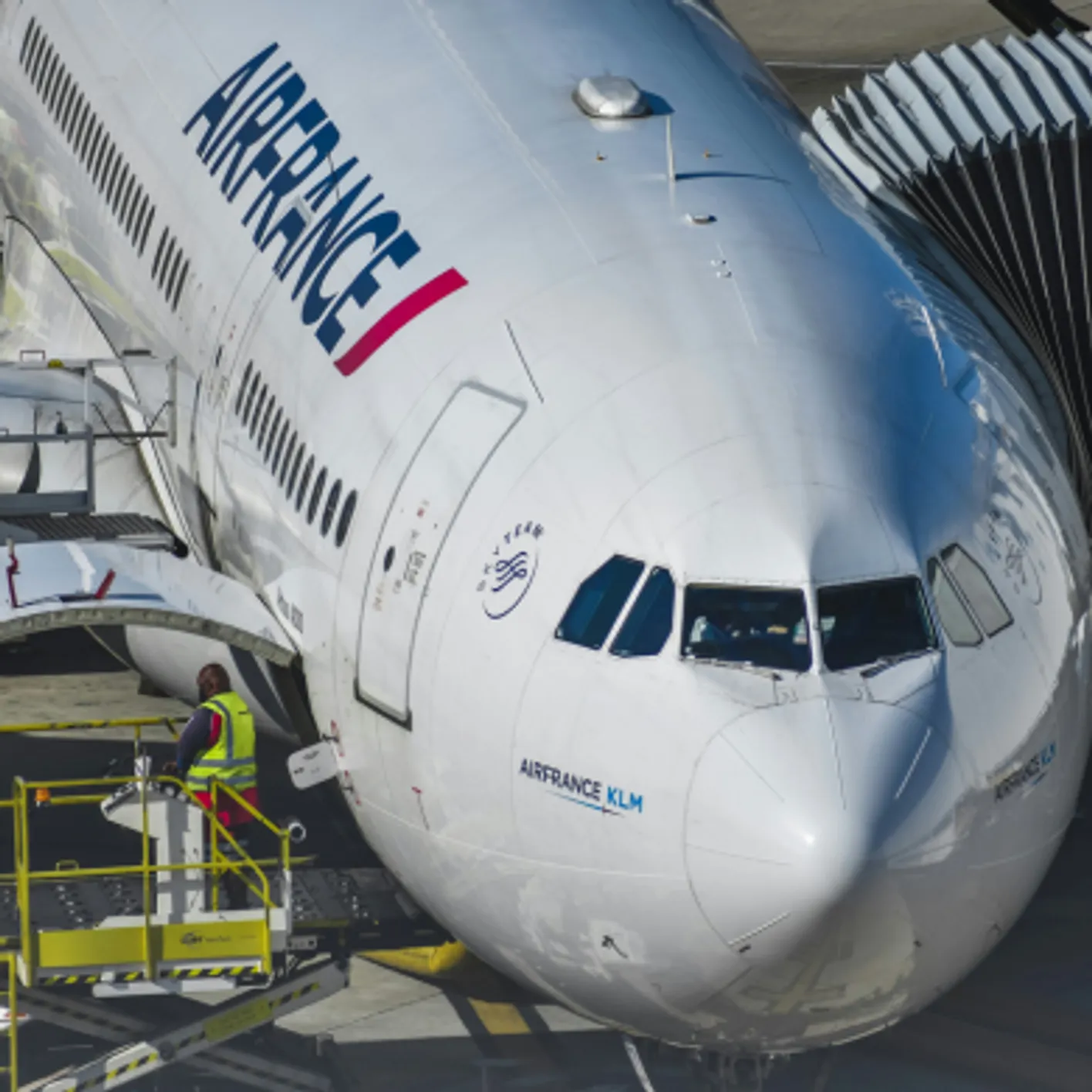an AirFrance white airplane preparing for departure. A man wearing a yellow shirt does the refuel.
