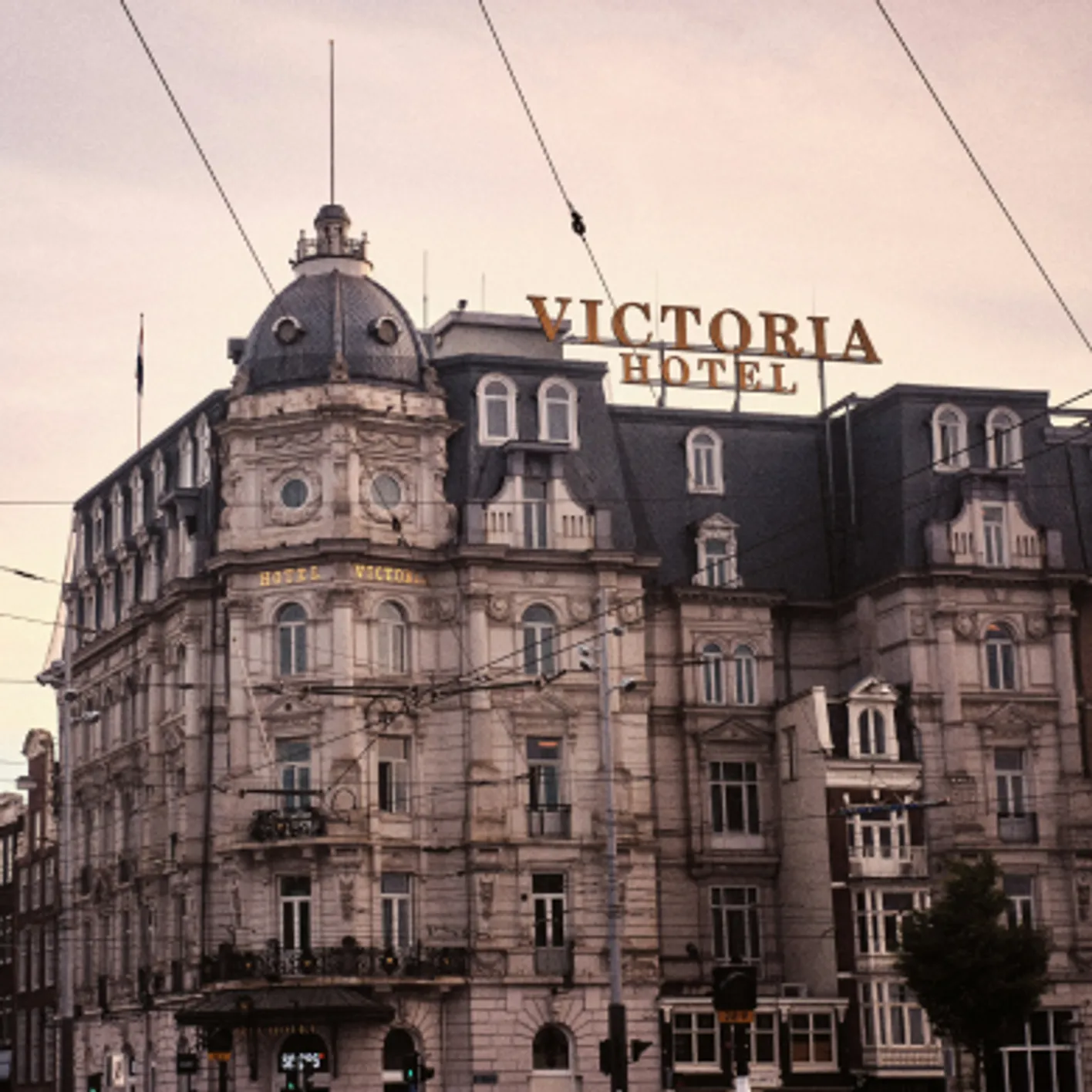A luxury high hotel in the twilight. It is white and grey. On the top, it is written Victoria Hotel.