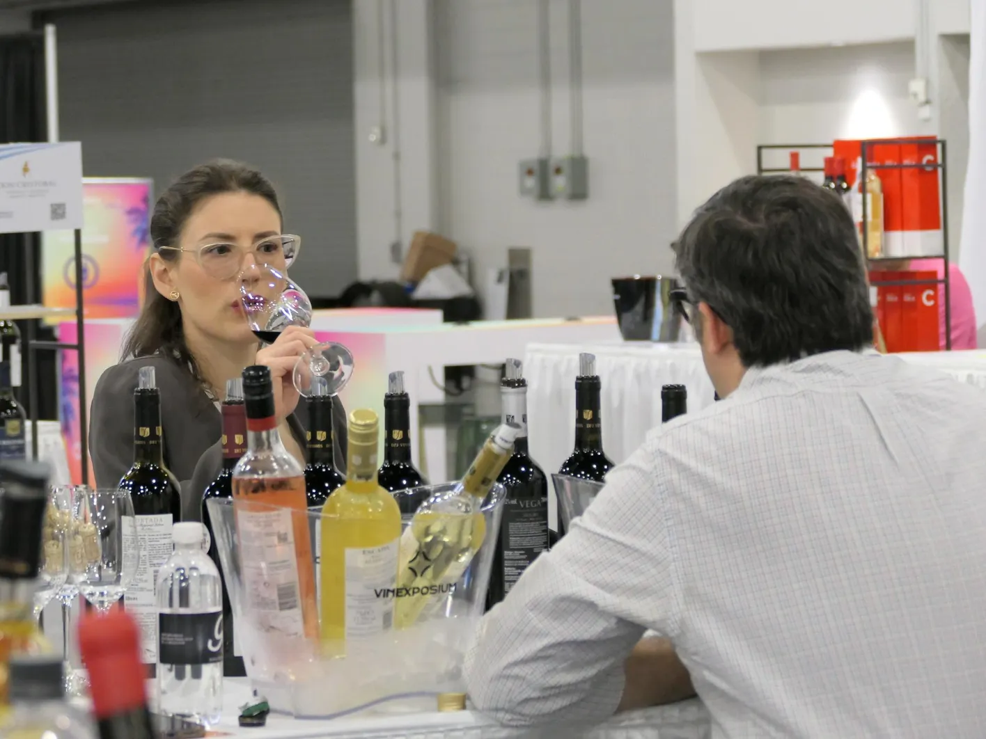 A woman is tasting a wine while an exhibitor is talking to her.