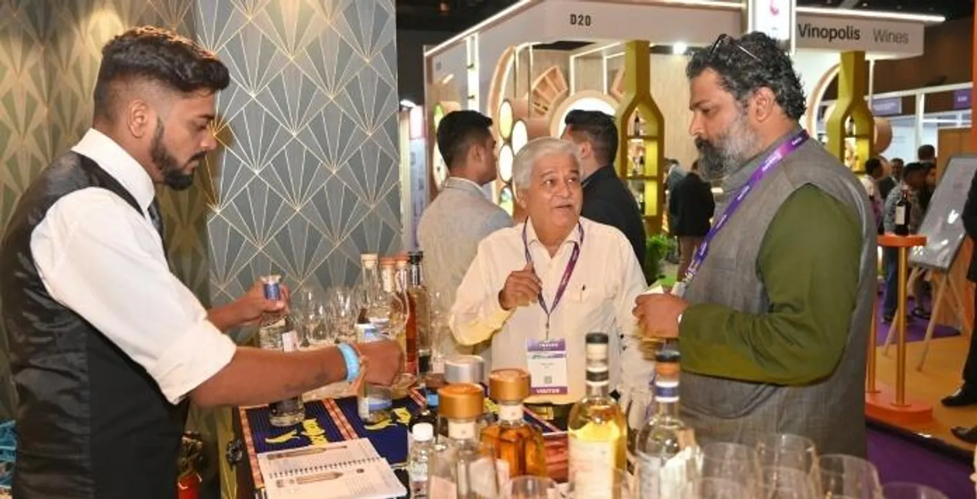 Indian men are talking during Vinexpo India. One is offering a glass of wine to the others.