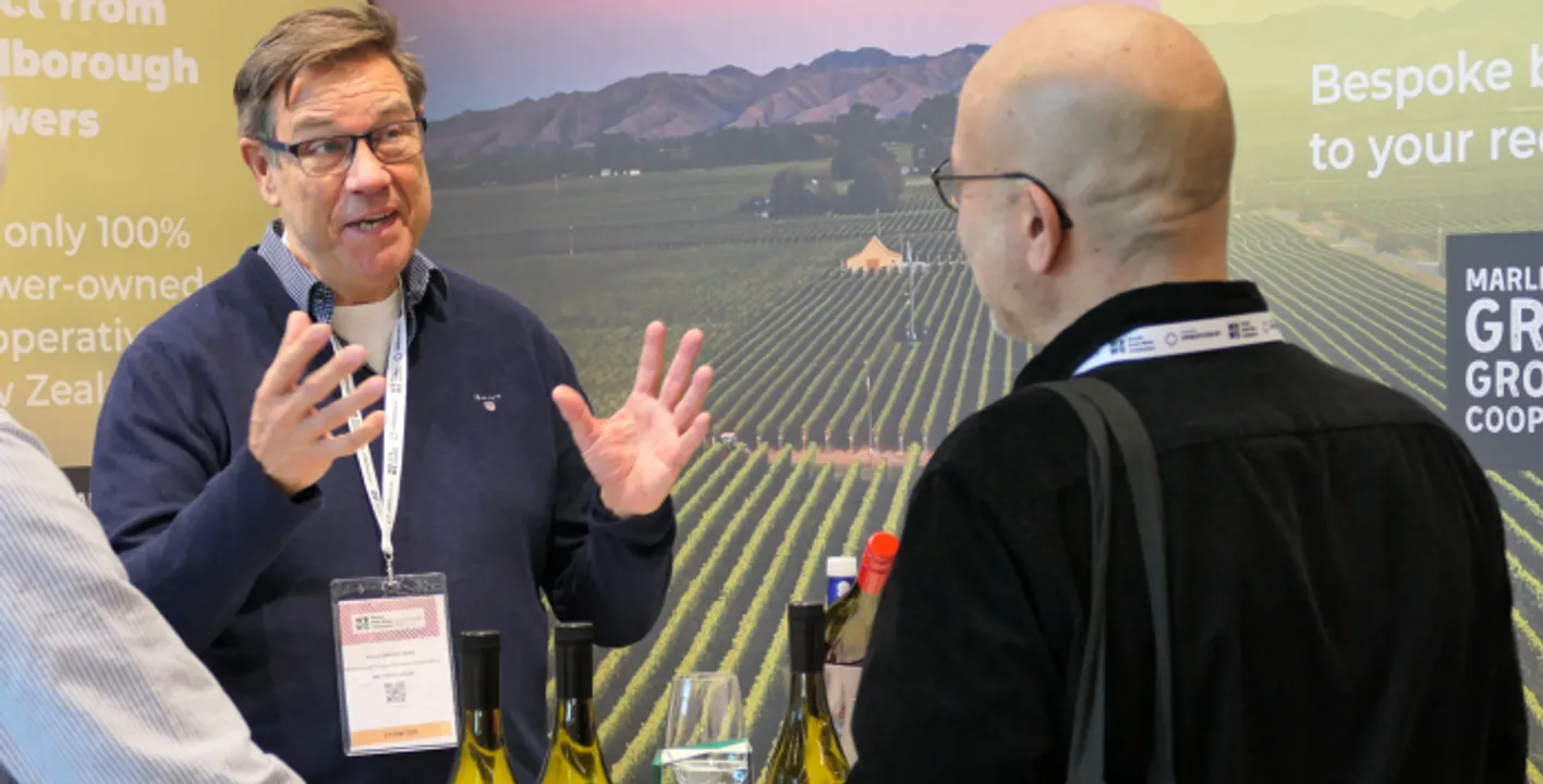 People who are talking about a bottle of bulk wine. A man is holding a a bottle to an exhibitor.