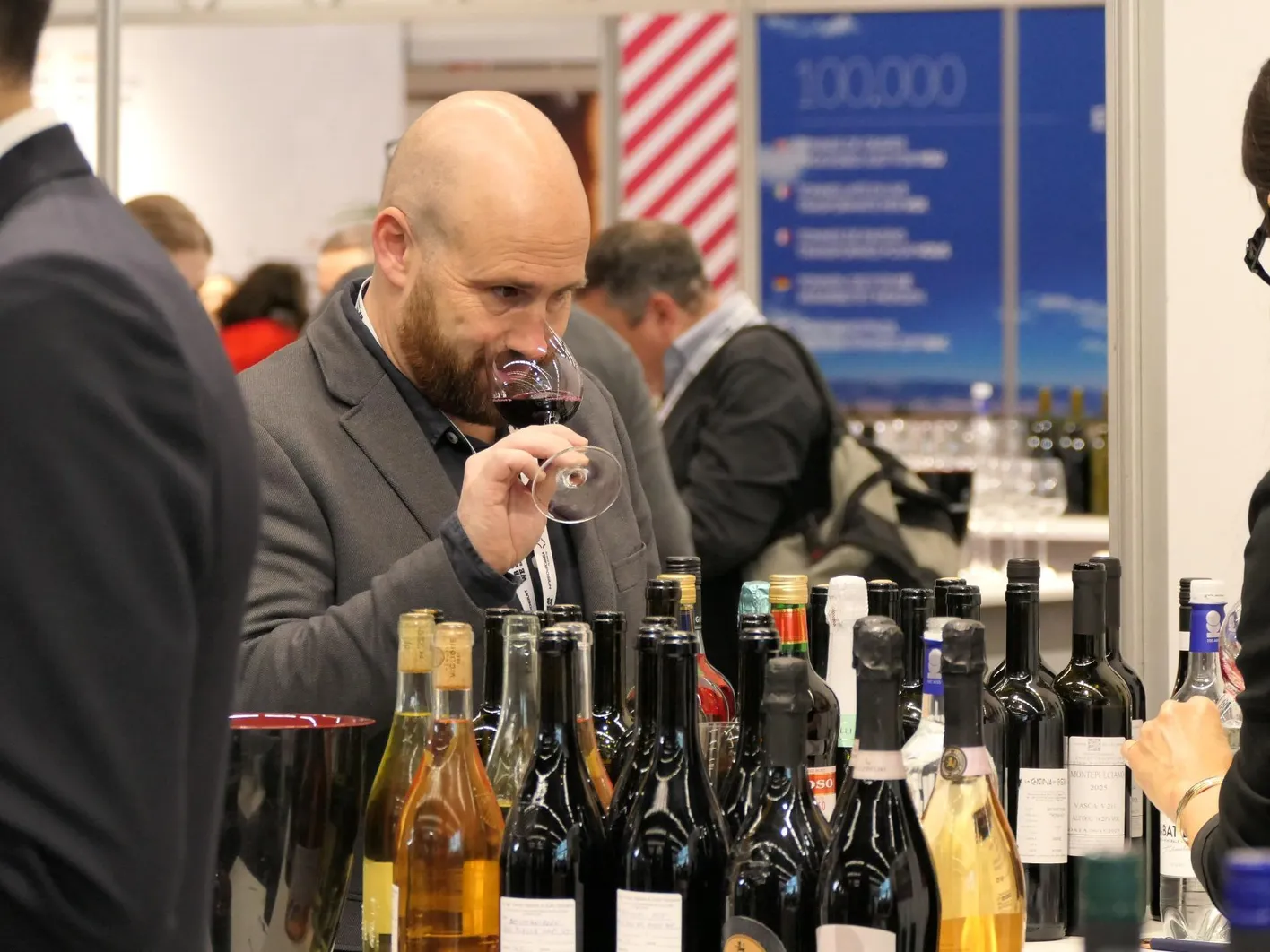 A woman who is taking a sip of a wine. In front, there are many wine bottles.