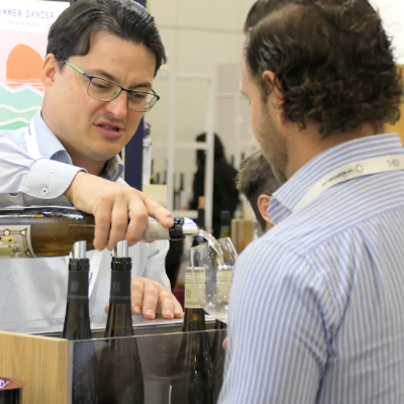 An exhibitor who is pouring some wine on a visitor's glass to taste it during Vinexpo Americas.