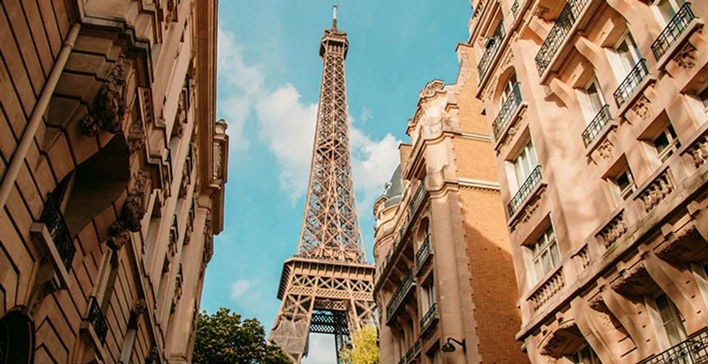 Eiffel Tower seen from a Paris street lined with buildings.